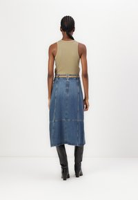 Oliven grønn uten ermer topp kombinert med en lys blå denim midi-skjørt og svarte hælte støvler, som viser en enkel design og strukturert form.