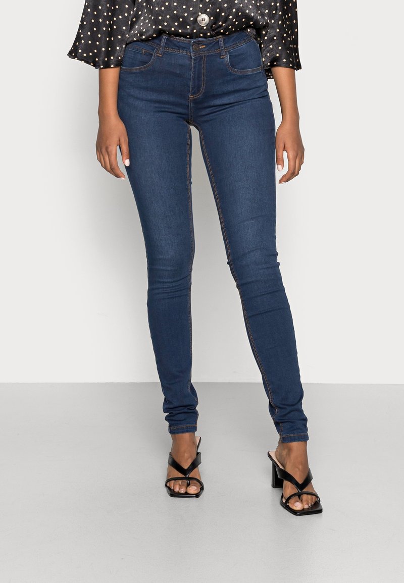 Slim jeans i mörkblå denim med kontrastsömmar, högmidjad design och en slät yta. Matchas med svarta remsandaler.
