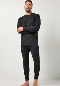 Sort langærmet bluse og tætsiddende bukser lavet af et blødt stof, med et enkelt design, rund halsudskæring og minimale syninger.