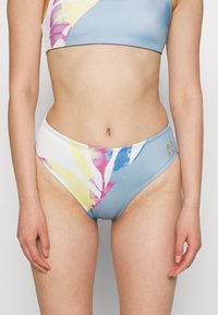 Parte de baixo de fato de banho com um padrão azul, branco e multicolorido em tons pastéis. Apresenta um design de corte alto com o logótipo da Roxy em elementos dourados.