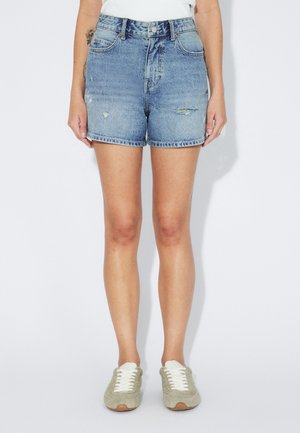 Jasnoniebieskie szorty jeansowe z postrzępionym brzegiem, wysokim stanem i przetarciami. Do tego miękkie zielone trampki z białymi sznurowadłami.