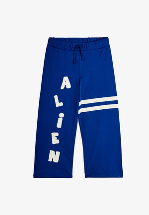 Pantaloni albaștri cu picioare largi, talie elastică și șnur, având litere albe "ALIEN" vertical pe piciorul stâng și două dungi albe pe piciorul drept.