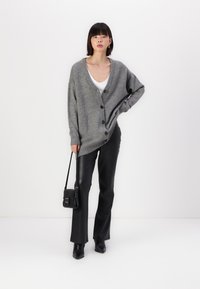 Cárdigan gris de punto con un escote en V profundo, seis botones negros, combinado con pantalones de piel negros y un pequeño bolso cruzado negro.