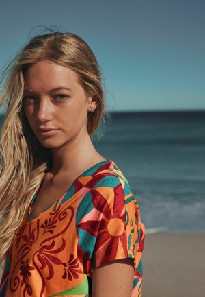 Värvikas lühikeste varrukatega särk oranži, mererohelise ja punase toonides, lille- ja geomeetriliste mustritega. Pehme kangas; V-kaelusega disain. Mereranna taust.