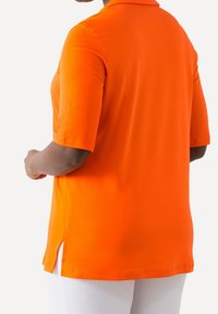 Orange polotröja med korta ärmar, sidoklipp och en slät textur. Utformad för en avslappnad passform och modern stil.