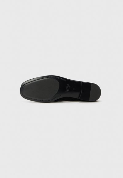 Semelle en cuir noir, avec une texture lisse, une forme arrondie et un logo discret, dotée d'un bord cousu et d'une zone de talon surélevée.
