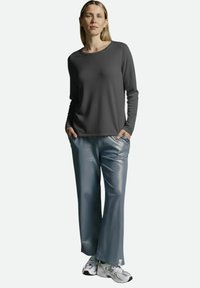 Graues Langarmshirt mit rundem Ausschnitt, kombiniert mit glänzenden, blau bedruckten, weiten Hosen und weißen Turnschuhen. Einfaches und funktionales Design.