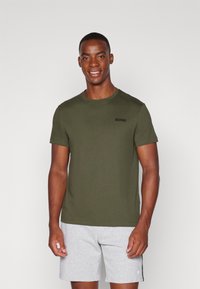 Oliven grøn bomulds-t-shirt med korte ærmer, rund halsudskæring og sort logo på brystet, parret med grå sportsbukser.