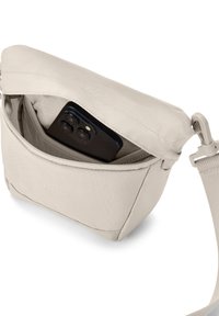 Világos bézs színű, puha anyagból készült crossbody táska, cipzáras zsebbel, benne egy okostelefonnal és leválasztható pánttal.