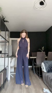 Sötétkék, nyakba akasztható overall, kulcslyuk részlettel, testhez simító derékkal és széles lábakkal. Puha, árnyékos anyag, enyhe fényességgel.