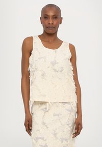 Strukturert off-white ermeløs topp med båtutringning, med frynsete kanter og løs design, sammen med en tilsvarende strukturert skjørt.