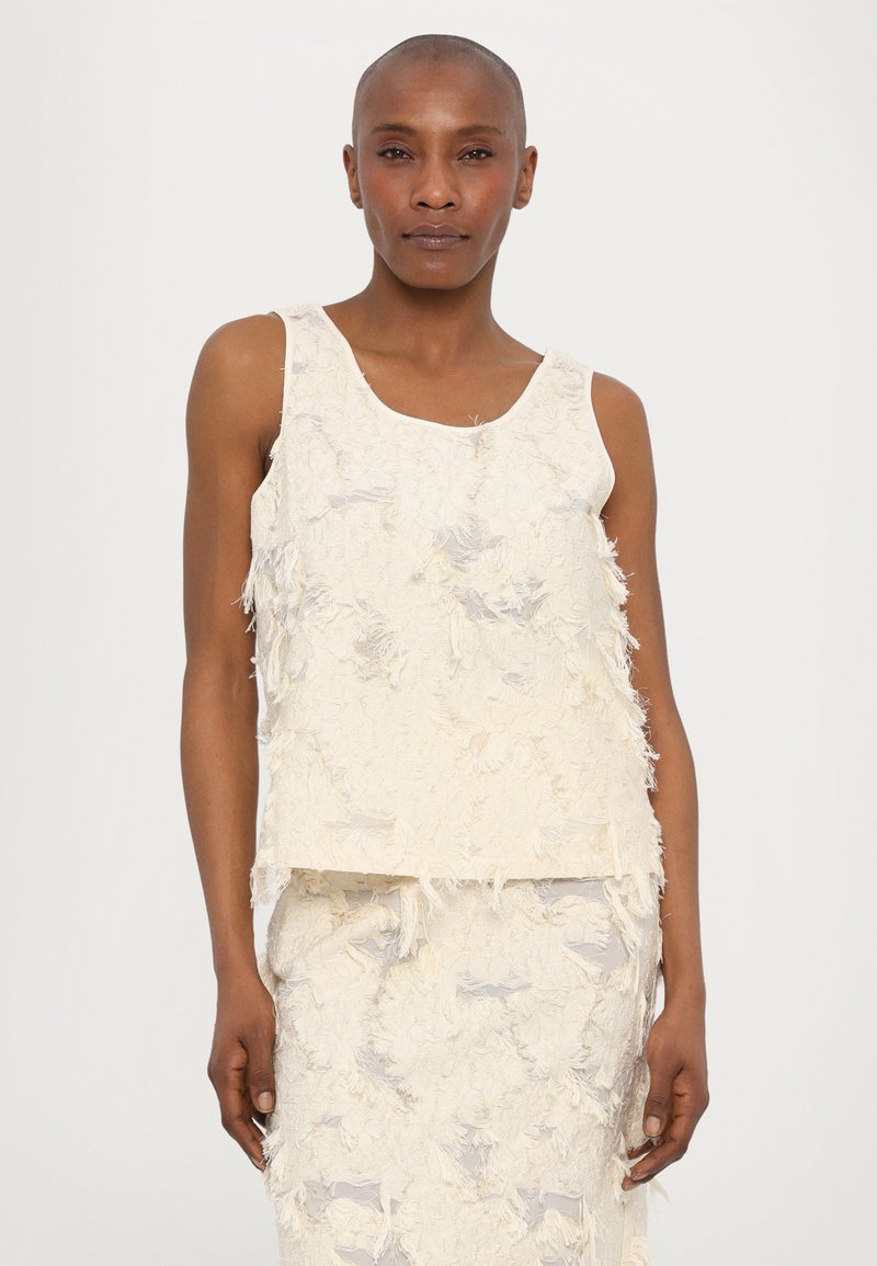 Gestructureerd off-white mouwloos topje met een bateauhals, voorzien van rafelige randen en een losse uitstraling, gecombineerd met een vergelijkbare gestructureerde rok.