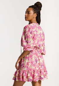 Kukallinen mekko puff-hihnoilla, jossa on sekoitus vaaleanpunaisia, purppuran, ja vihreitä kuvioita. Pitsireunus ja joustava vyötärö antavat istuvan siluetin.