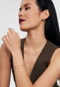 Zestaw biżuterii wykonany z złota, w skład którego wchodzą naszyjnik, kolczyki i bransoletka z kolorowymi kamieniami szlachetnymi, prezentujący delikatny powiązany wzór i błyszczące akcenty.