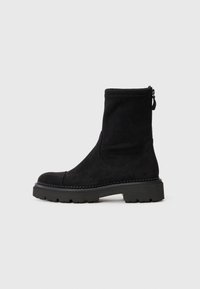 Bottine en suede noir avec un bout rond, semelle en caoutchouc épaisse et fermeture éclair sur le côté. Design simple avec des détails de couture subtils autour de la semelle.
