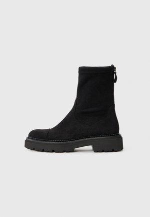 Bottine en suede noir avec un bout rond, semelle en caoutchouc épaisse et fermeture éclair sur le côté. Design simple avec des détails de couture subtils autour de la semelle.