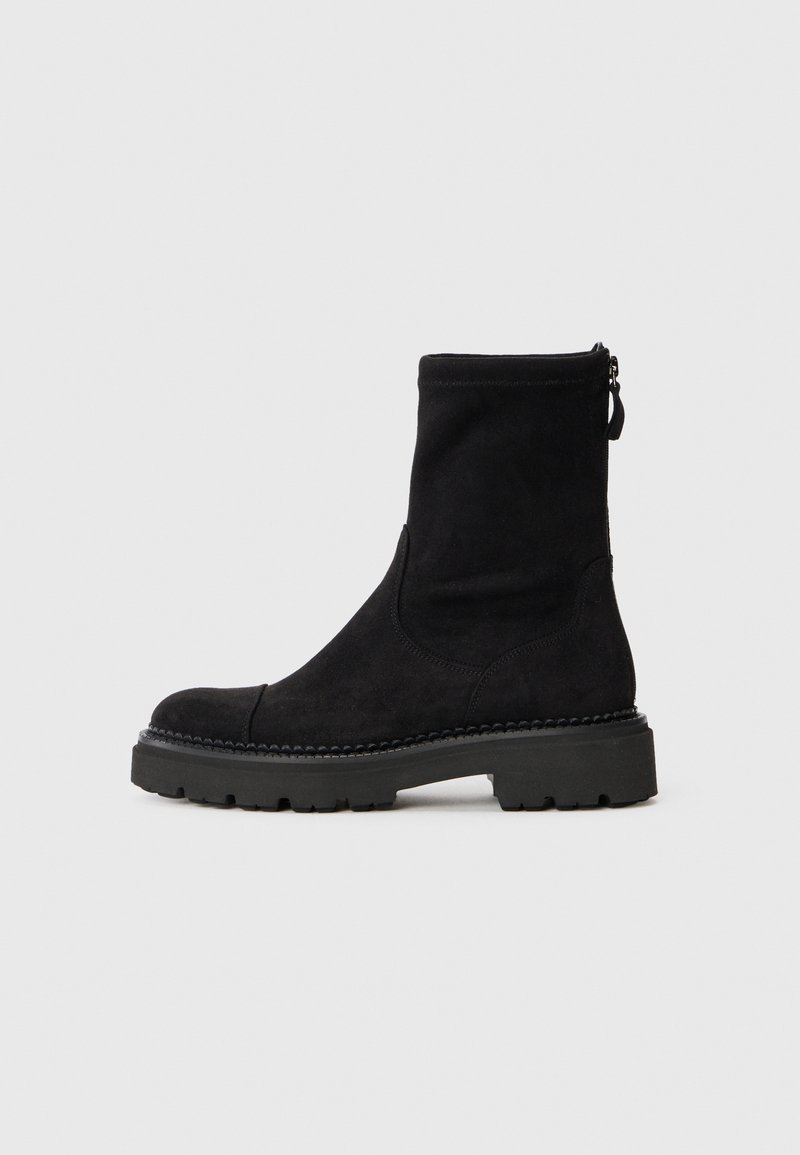 Bottine en suede noir avec un bout rond, semelle en caoutchouc épaisse et fermeture éclair sur le côté. Design simple avec des détails de couture subtils autour de la semelle.