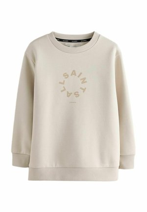 Sweatshirt beige clair en tissu doux, avec un col rond et des poignets côtelés. Texte graphique central dans un design circulaire.