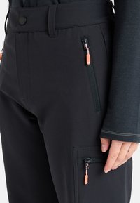 Czarne spodnie o sportowym kroju, wykonane z elastycznego materiału, z zamykanymi na zamek kieszeniami z pomarańczowymi uchwytami i eleganckim, dopasowanym krojem.