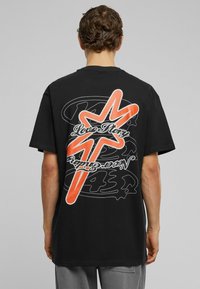 Sort bomulds t-shirt med et stort orange grafisk design på ryggen med teksten "Love Story" og svungne sorte konturer.