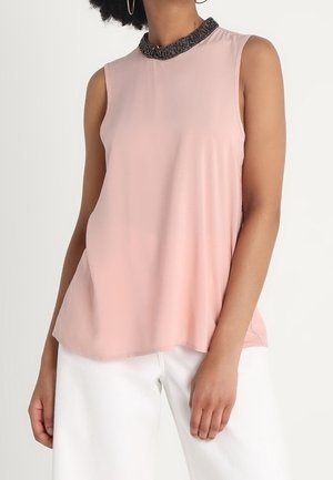 Ærmeløs lyserød bluse med udsmykket sort krave, båret med hvide bukser, vist fra nakke til hofter.