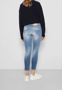 Úzké modré džíny s vybledlým povrchem, zadní kapsy se stehováním, nošené s černým žebrovaným svetrem a bílými teniskami.