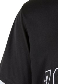 Maillot de sport noir en tissu texturé. Présente un numéro "72" blanc imprimé à l'avant, avec des rayures blanches et noires contrastantes au niveau de l'ourlet.