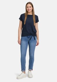 Mørkeblå kortærmet top med en knyttet frontdetalje, parret med lyseblå slim jeans og hvide sneakers. Enkel, afslappet design.