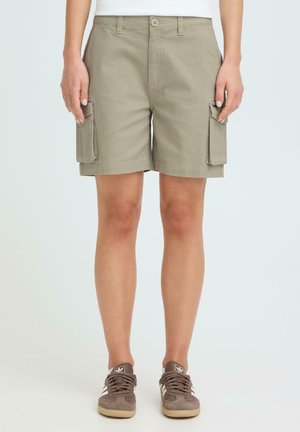 Osoba nosząca khaki cargo spodenki do kolan z przednim guzikiem i bocznymi kieszeniami, zestawione z brązowymi tenisówkami.