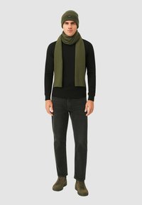 Berretto e sciarpa in maglia verde indossati con una maglietta nera a maniche lunghe, jeans neri e sneakers verde scuro, caratterizzati da una vestibilità slim e una texture morbida.