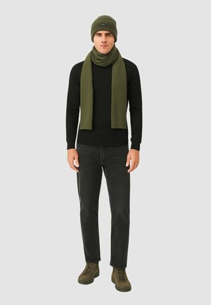 Berretto e sciarpa in maglia verde indossati con una maglietta nera a maniche lunghe, jeans neri e sneakers verde scuro, caratterizzati da una vestibilità slim e una texture morbida.