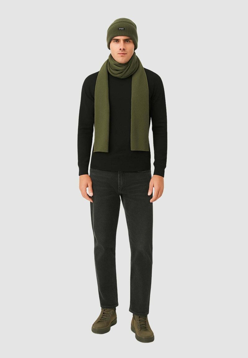 Berretto e sciarpa in maglia verde indossati con una maglietta nera a maniche lunghe, jeans neri e sneakers verde scuro, caratterizzati da una vestibilità slim e una texture morbida.