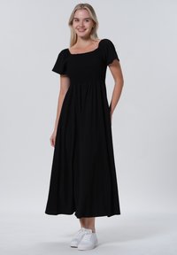 Svart maxiklänning med korta puffärmar, elastisk bodice och flödande kjol. Bärs med vita sneakers och har en avslappnad, casual design.