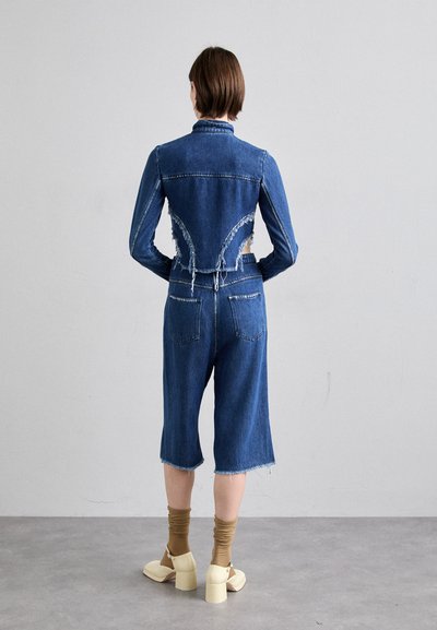 Denim jumpsuit med en avkortet jakke og vide shorts, med frynsete kanter og kontraststing. Brukt med brune knelang sokker og lette sko.