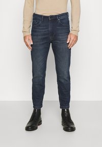 Mörkblå denimjeans med slim fit, med midjehöjd, fem fickor och kontrasterande sömmar, matched med svarta snörkängor.