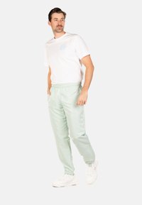 Hellgrüne Jogginghosen mit einem elastischen Bund, Seitentaschen und einem dezenten Logo auf dem linken Oberschenkel, kombiniert mit einem weißen T-Shirt.