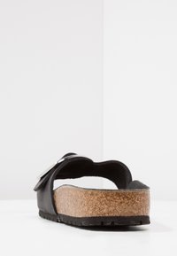 Svart lädersandal med korkfotbädd, utrustad med en bakslinga och silverfärgad spänneaccent. Texturerad sula med synligt mönster.