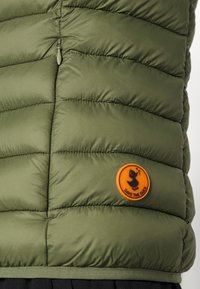 Chaleco inflado verde con diseño acolchado, que presenta un dobladillo negro y un parche de goma naranja etiquetado "SAVE THE DUCK" con un gráfico de un pato.