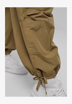 Khaki katonai nadrág elasztikus mandzsettával, oldalzsebekkel és puha tapintással, fehér sportcipőkkel párosítva. Kényelmes dizájn, amely alkalmas a mindennapi viseletre.