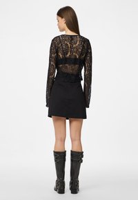 Crna čipkasta bluza dugih rukava s prozirnim leđima i elastičnom trakom u struku, u kombinaciji s crnom mini suknjom i crnim čizmama do koljena s kopčama.