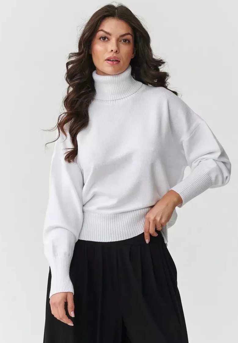 Biały sweter z golfem, z prążkowanymi mankietami i dołem, o luźnym kroju i długich rękawach, w połączeniu z czarnymi spodniami plisowanymi.