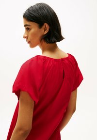 Vestido rojo de manga corta con un diseño fluido, escote fruncido y cierre con botones en la espalda. Textura suave y tela ligera.