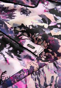 Tuvas tuvplāksne ar ziedu rakstu audumā violetos, rozā, melnos un krēma toņos, ar izšūtu kabatu un mazu metāla birku ar uzrakstu "NEXT."