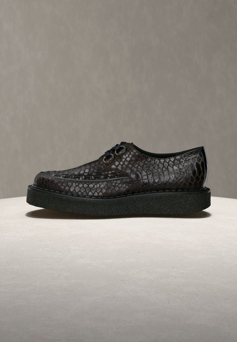 Dunkelbrauner Lederschnürschuh mit strukturiertem Schlangenledermuster und dicker schwarzer Sohle auf einer hellen, runden Oberfläche.