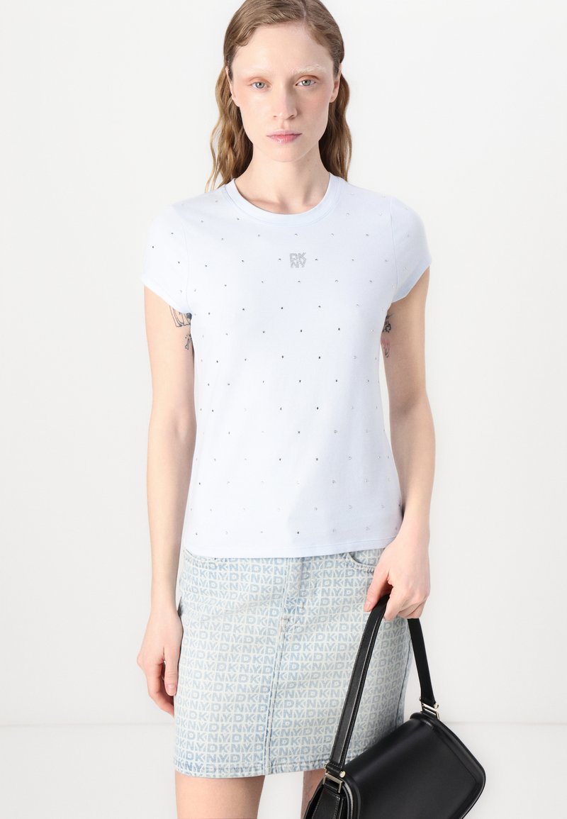 T-shirt di cotone azzurro chiaro con maniche corte, caratterizzata da un sottile motivo a pois e un logo sul petto. Abbinata a una gonna di jeans a motivi.