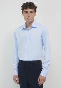 Helles blaues Langarmhemd mit klassischem Kragen, Knopfverschluß und glattem Stoff. Kombiniert mit dunklen Hosen. Schlichtes, elegantes Design.