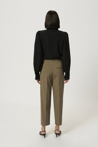 Blusa nera plissettata a maniche lunghe abbinata a pantaloni beige a righe sottili. Il modello indossa scarpe con tacco kitten nere. Sfondo pulito e minimalista.