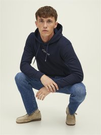 Hanorac din bumbac bleumarin cu cordon, cu un logo pe partea din față. O pereche de blugi din denim bleu deschis și pantofi din suede bej cu vârful rotunjit.