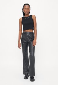 Zwarte cropped tanktop gecombineerd met high-waisted zwarte neplederen broek. Gladde textuur met een recht gesneden ontwerp en minimale hardware.