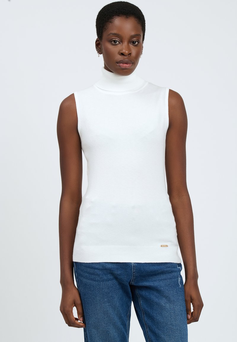 Maglione senza maniche bianco con collo alto, orlo a coste e dettagli laterali. Tessuto morbido con una trama liscia. Abbinato a jeans di denim blu.